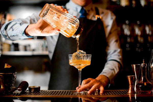 barman gently pours finished cold cocktail from glass shaker int